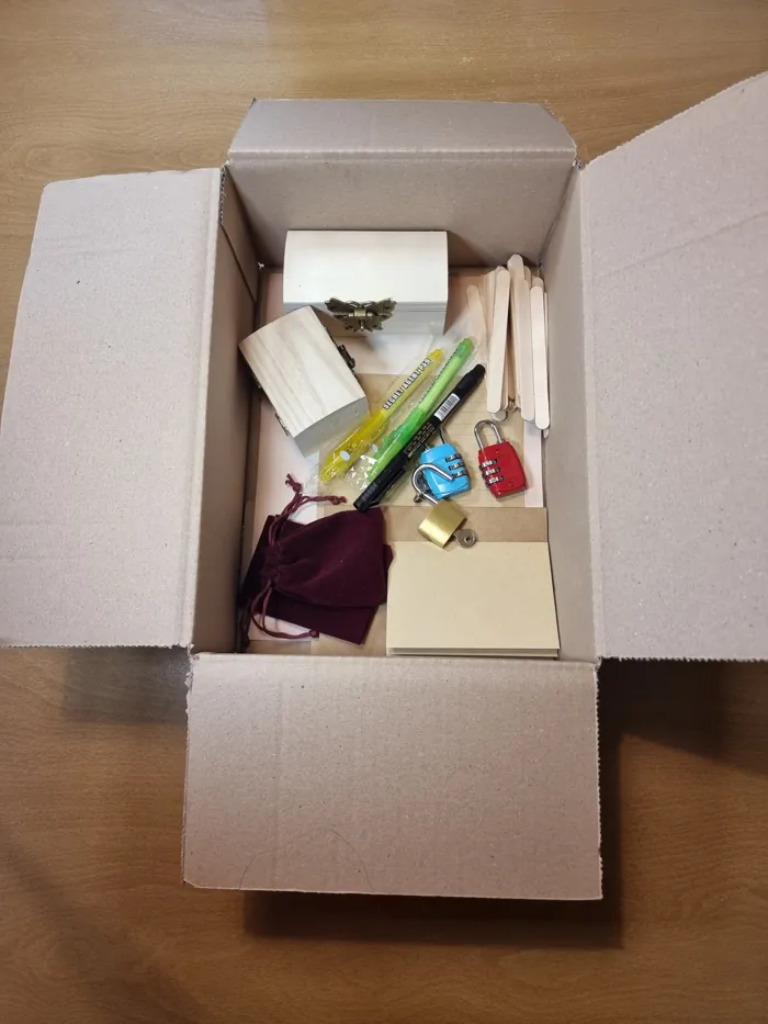Een geopende doos met een houten kistje, sloten, pennen, enveloppen en een rood zakje